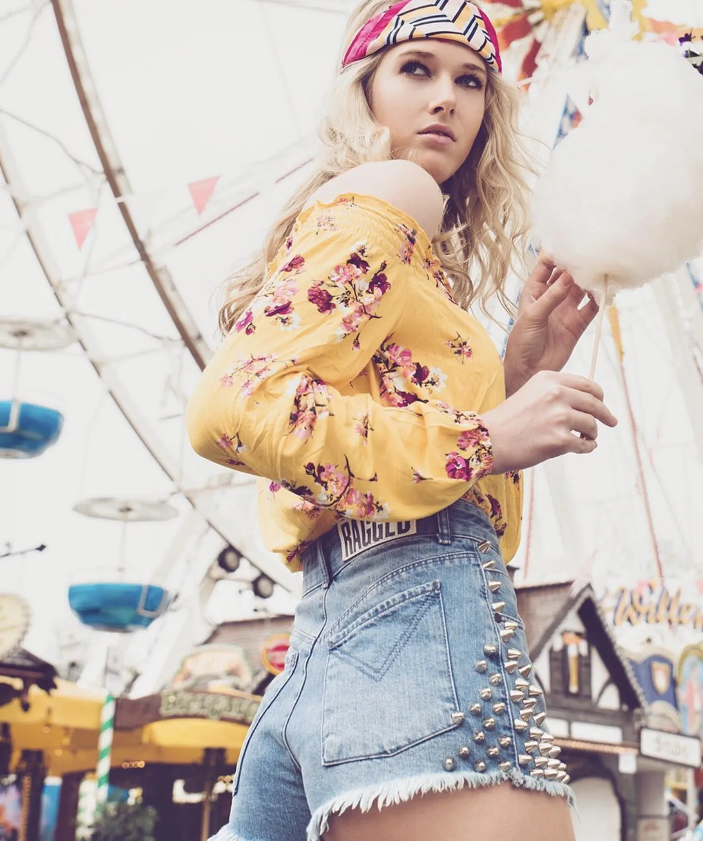 Frau in Jeansshorts mit Zuckerwatte vor dem Riesenrad