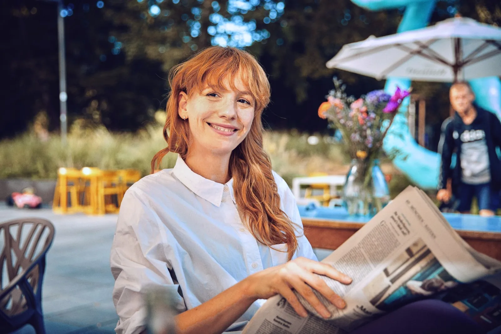 Laura im weißen Hemd mit Zeitung im Straßencafé