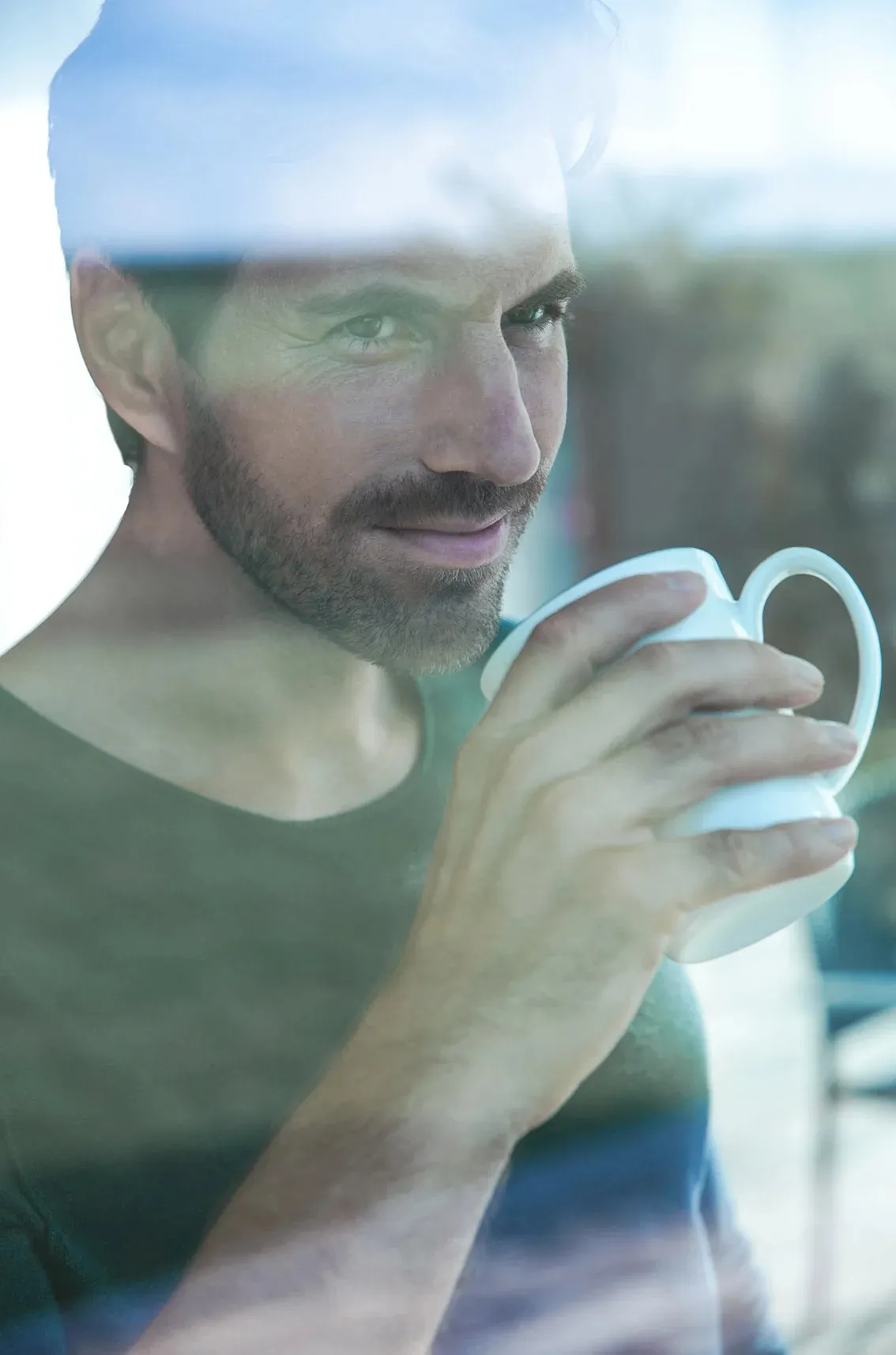 Mann mit Kaffeetasse hinter einer Fensterscheibe
